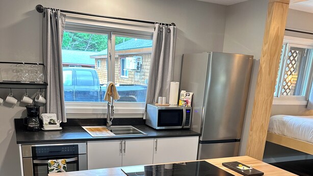 A compact kitchen with a wooden countertop, a built-in microwave, a stainless steel refrigerator, and a sink. There are two stools at the counter. - North Coast Place (Marquette)