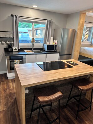 A compact kitchen with a wooden countertop, a built-in microwave, a stainless steel refrigerator, and a sink. There are two stools at the counter. - North Coast Place (Marquette)