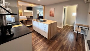 A modern kitchen with a central island, wooden flooring, and a dining area with a chair. - North Coast Place (Marquette)
