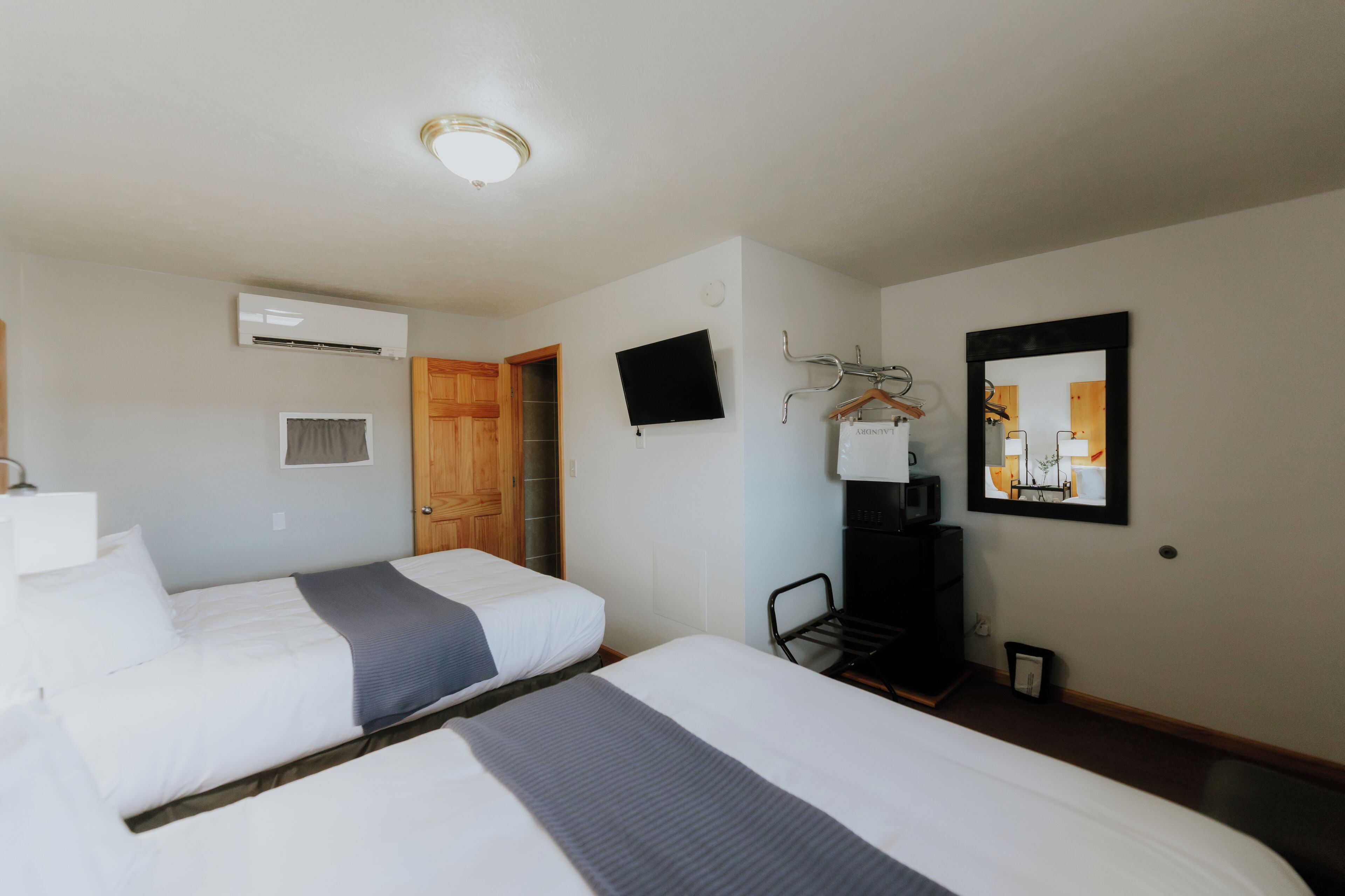Ein Hotelzimmer mit zwei Betten, einem Fernseher, einer Klimaanlage, einer Holztür, einem Spiegel und einem Kleiderständer.