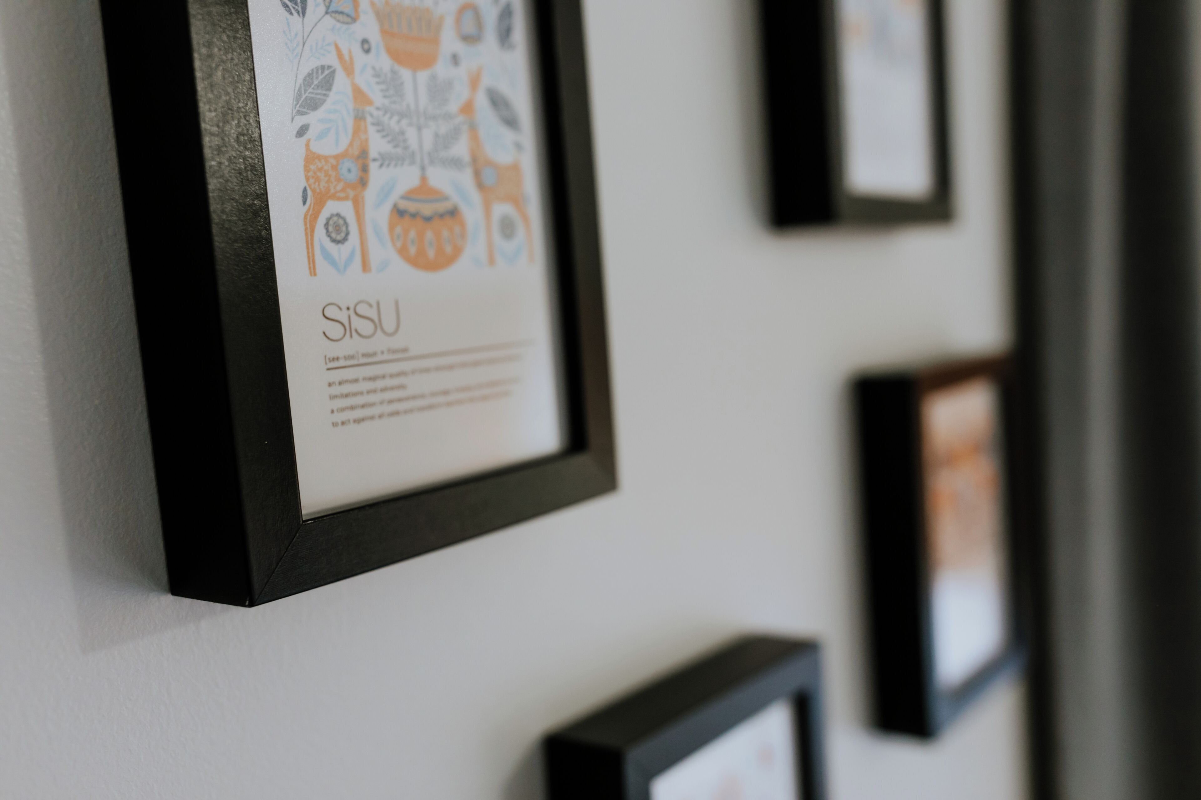 A wall with framed artwork, including a piece with a deer and floral design and the word "SiSU" below it.