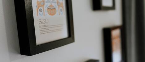 A wall with framed artwork, including a piece with a deer and floral design and the word "SiSU" below it.