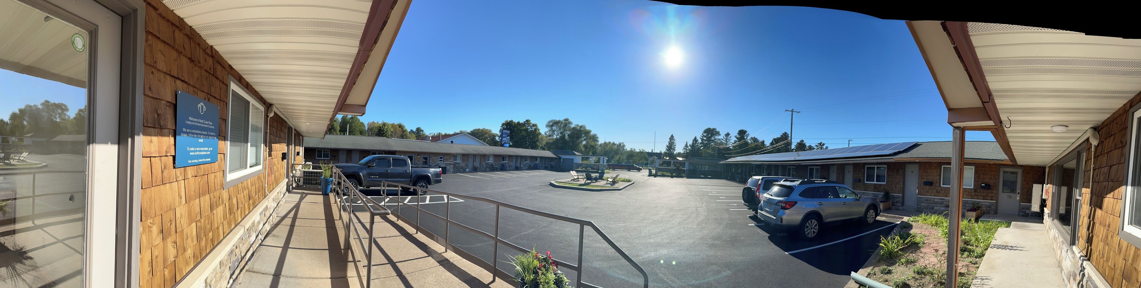 A parking lot with several cars, a building with a wooden facade, and a clear blue sky.