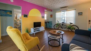 Ein Wohnzimmer mit Sofa, Sessel und Couchtisch, einem Fernseher und einem Fahrrad.