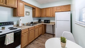 A compact kitchen with wooden cabinets, a white refrigerator, a stove, and a microwave. - 1BR Cocoa Beach Home - 1 Min to Beach! (Cocoa Beach)