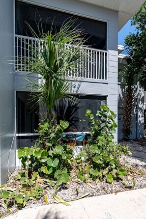 Un bâtiment moderne à deux étages, doté d’un balcon, entouré de différentes plantes et agrémenté d’une petite table.