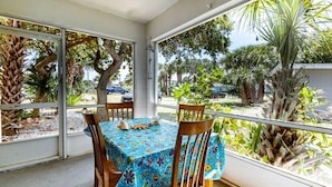 A balcony with a table and chairs, covered with a patterned tablecloth, overlooking a garden with trees and a parked car. - 1BR Cocoa Beach Home - 1 Min to Beach! (Cocoa Beach)