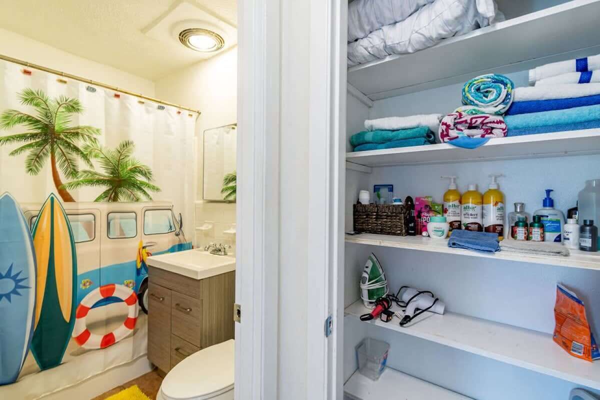 A bathroom with a shower curtain featuring palm trees, a toilet, and a shelf with toiletries.