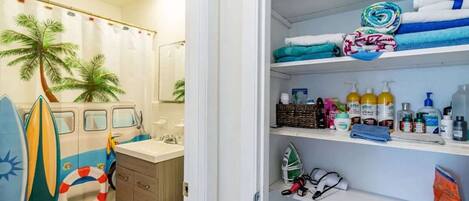 A bathroom with a shower curtain featuring palm trees, a toilet, and a shelf with toiletries.