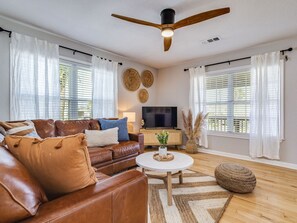 A living room with a brown leather sofa, a round coffee table, a ceiling fan, and a flat-screen TV.