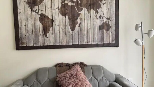 A grey sofa with a fluffy pink pillow and a world map artwork above it. - Cozy Riverfront Retreat Close to City (Mableton)