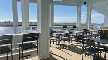Enjoy the serene view of the water from this outdoor patio, featuring comfortable seating and large windows for a peaceful retreat.