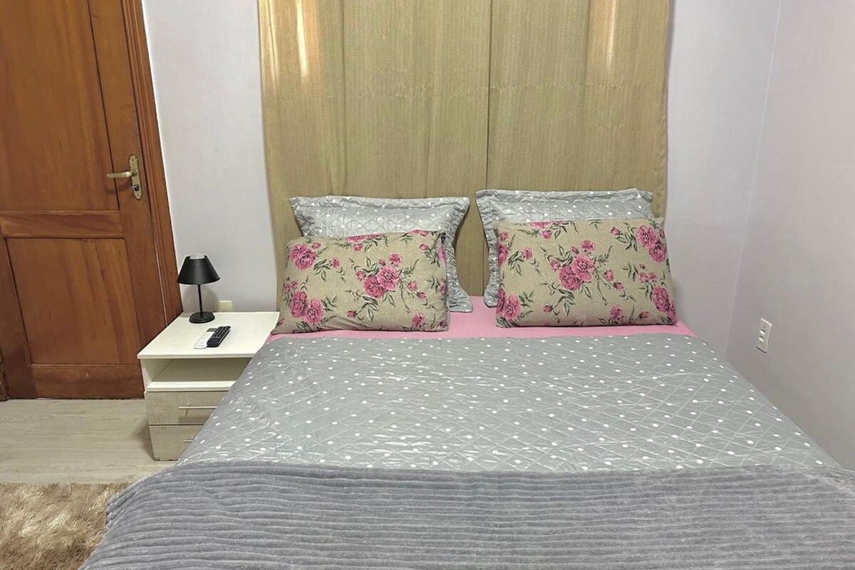 Un dormitorio con cama, dos almohadas, una mesita de noche con lámpara y una puerta de madera.