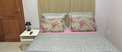 Un dormitorio con cama, dos almohadas, una mesita de noche con lámpara y una puerta de madera.