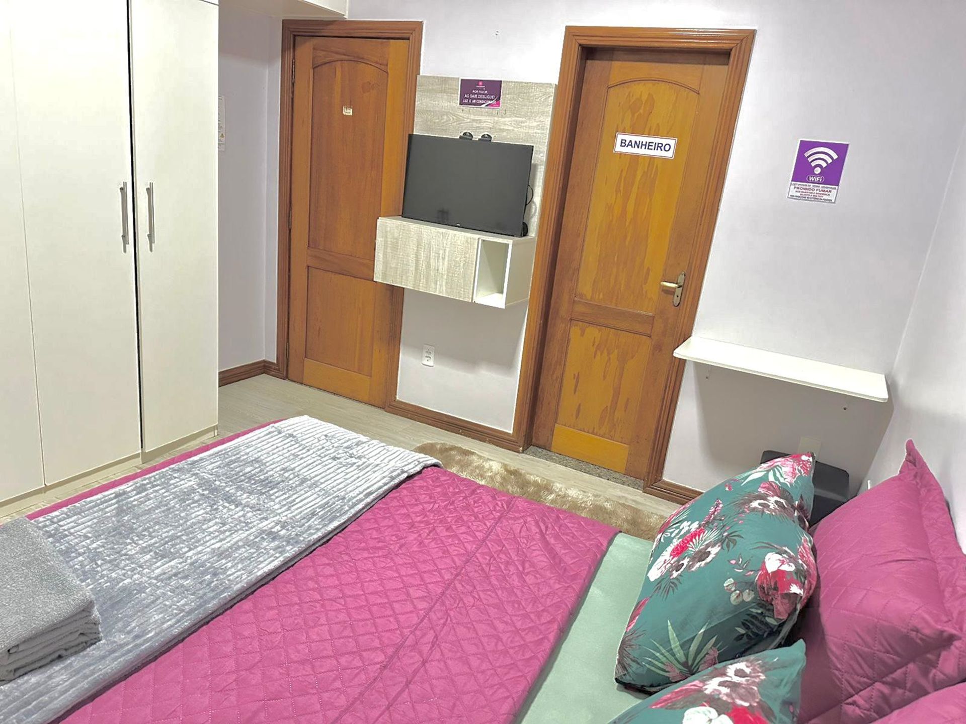 Ein Schlafzimmer mit Bett, Kissen, einem Kleiderschrank, einer Tür mit einem Schild und einem Wandregal.