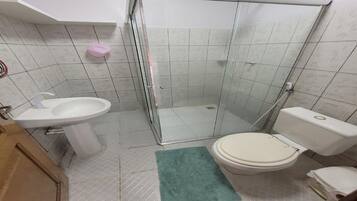 Un baño con cabina de ducha de vidrio, inodoro y lavamanos.