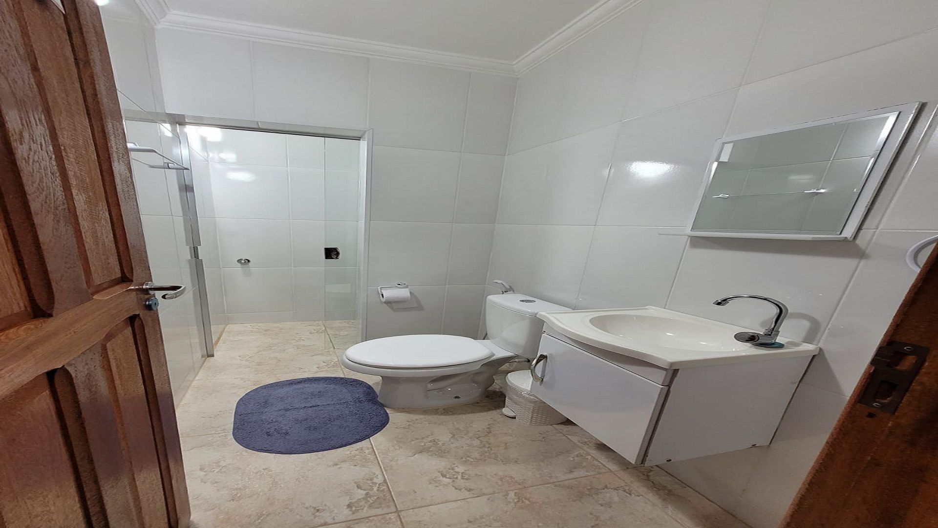 Baño con inodoro, lavamanos, espejo y zona de ducha.