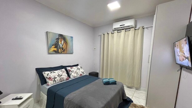 Ein Schlafzimmer mit einem Bett, einem Nachttisch, einem Fernseher, einer Klimaanlage und einem Bild an der Wand.