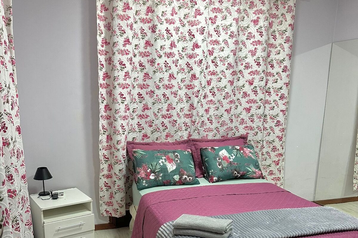Une chambre à coucher avec un lit, une table de chevet, une lampe et des rideaux à motifs floraux.