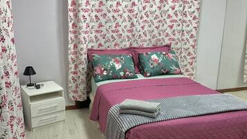 Un dormitorio con una cama, una mesita de noche, una lámpara y cortinas con motivos florales.