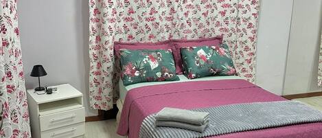 Un dormitorio con una cama, una mesita de noche, una lámpara y cortinas con motivos florales.