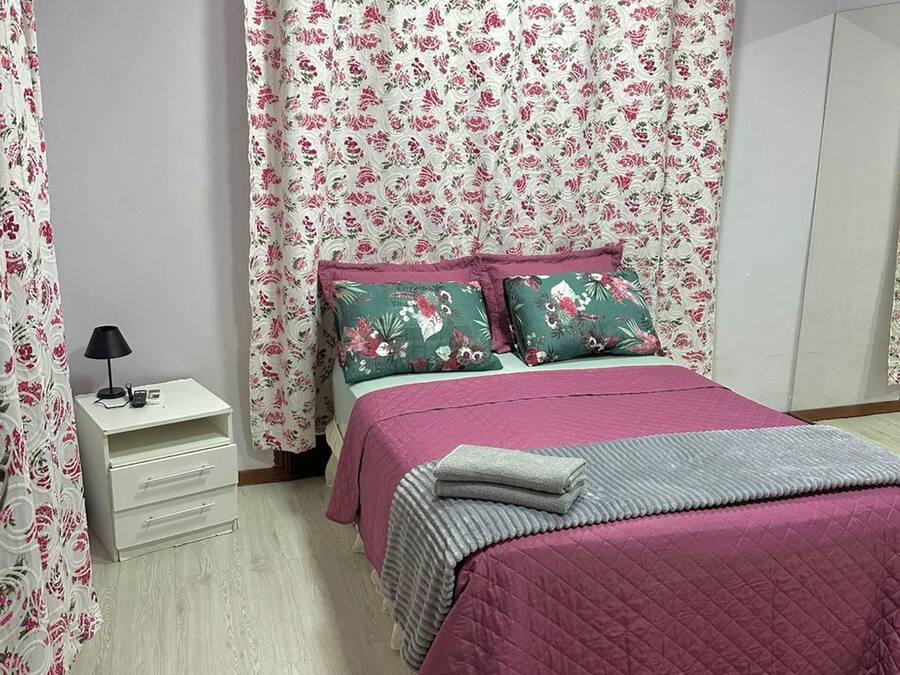 Un dormitorio con una cama, una mesita de noche, una lámpara y cortinas con motivos florales.