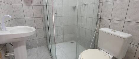 A bathroom with a glass shower enclosure, a white sink, a toilet, and a green bath mat.
