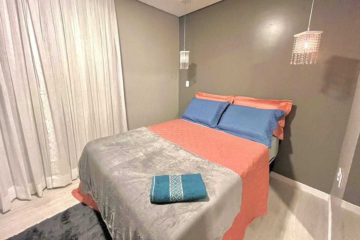 Een slaapkamer met een bed, gordijnen, een hanglamp en een wandlamp.