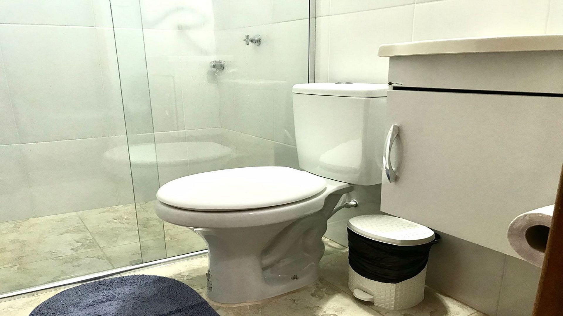 A bathroom with a toilet, a shower, and a trash bin.