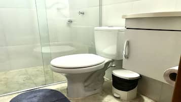 A bathroom with a toilet, a shower, and a trash bin.