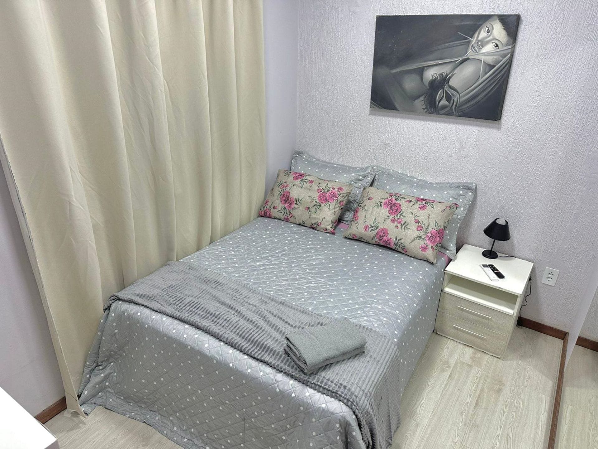 A bedroom with a bed, pillows, a nightstand, a lamp, and a painting on the wall.