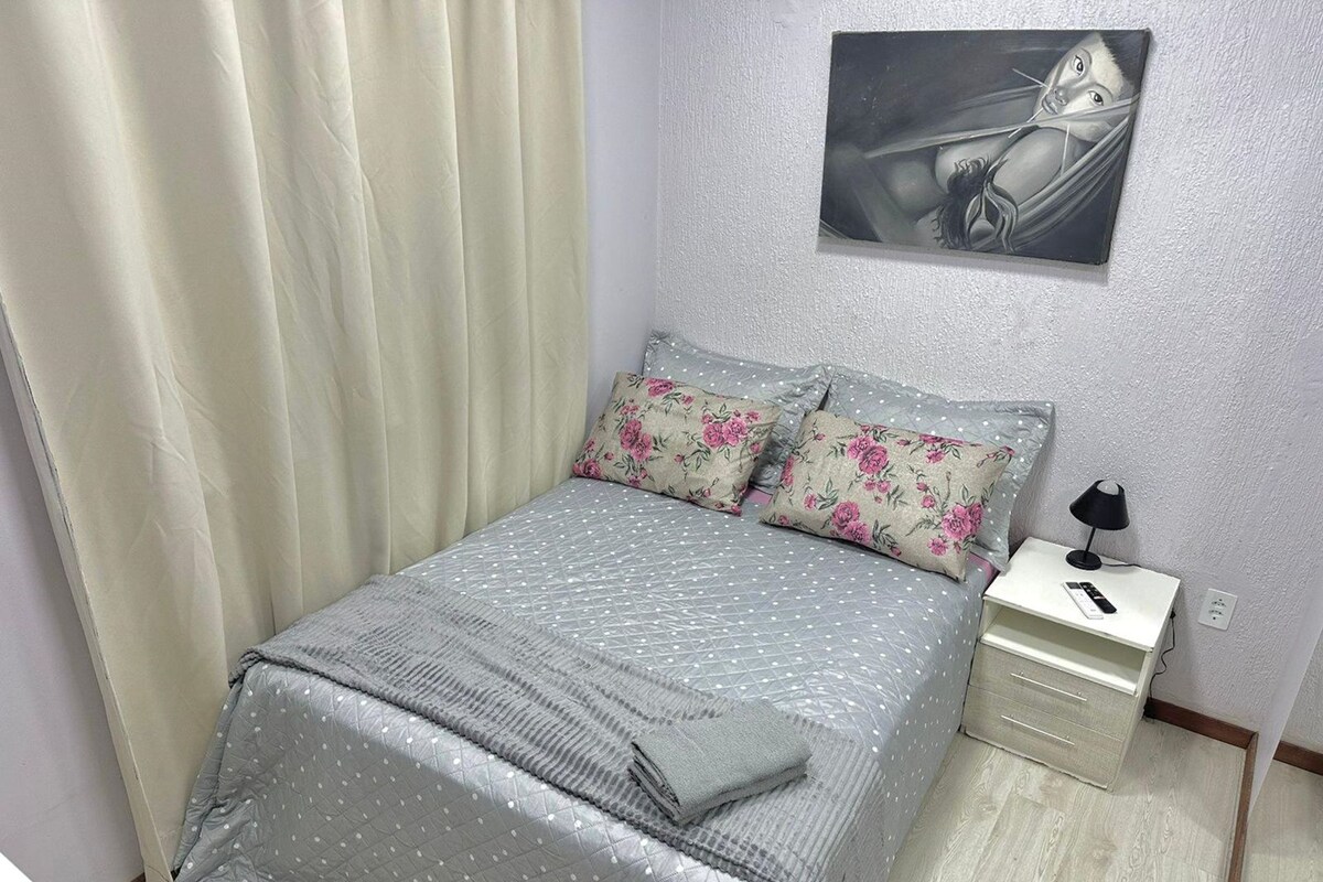 Une chambre à coucher avec un lit, des oreillers, une table de chevet, une lampe et un tableau au mur.