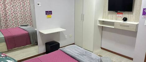 Un dormitorio con cama, armario, televisor y un pequeño escritorio.