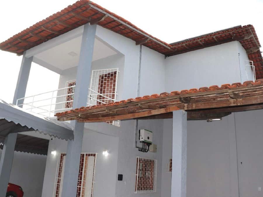 Un edificio blanco con techo de tejas rojas, un balcón y una zona cubierta con techo de lámina metálica.