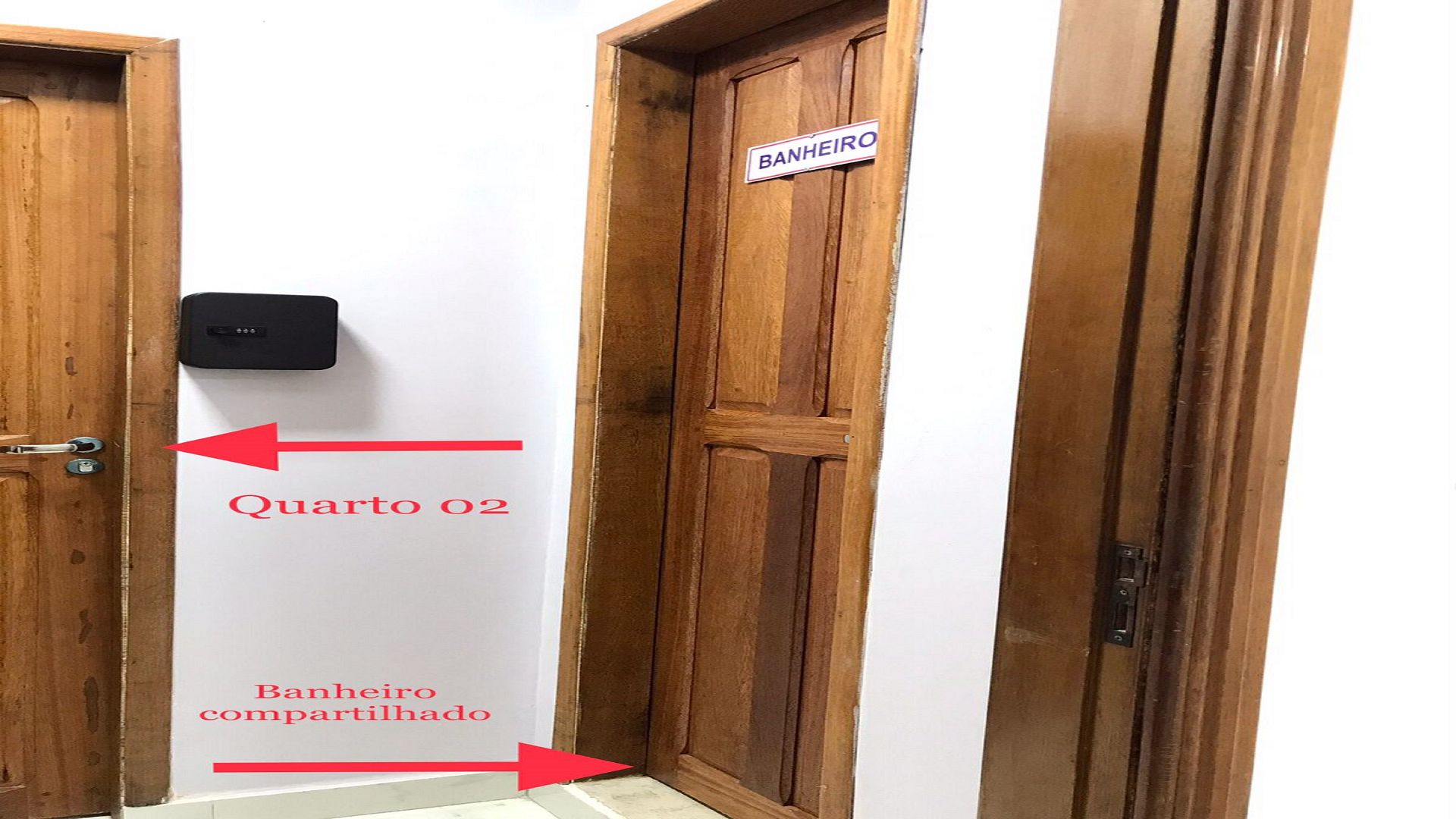 Una puerta de madera con un letrero que dice 'BANHEIRO compartilhado' y una flecha que indica 'Quarto 02'.