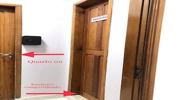 Una puerta de madera con un letrero que dice 'BANHEIRO compartilhado' y una flecha que indica 'Quarto 02'.