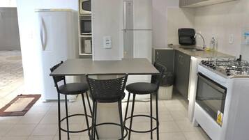 A kitchen with a white refrigerator, a stove, and two bar stools.