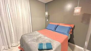 Een slaapkamer met een bed, gordijnen, een hanglamp en een wandlamp.
