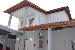 Un bâtiment blanc avec un toit recouvert de tuiles rouges, un balcon et une zone couverte dotée d’un toit en tôle ondulée.