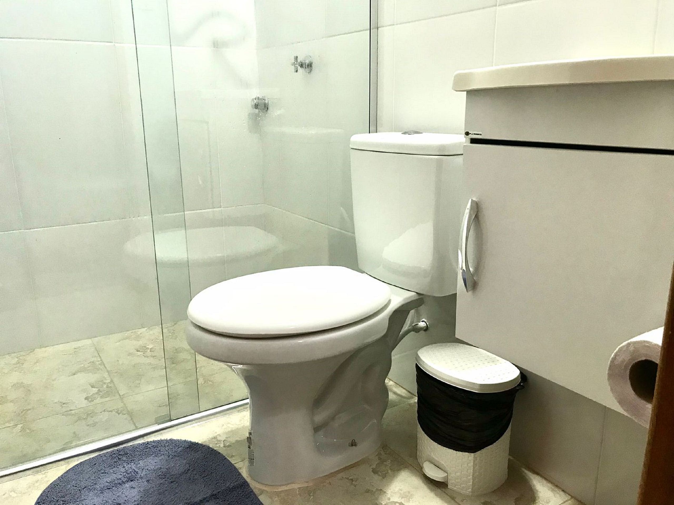 A bathroom with a toilet, a shower enclosure, and a trash bin.