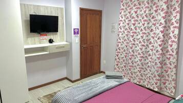 A bedroom with a bed, a TV mounted on a wall, a wooden door, and a floral curtain.