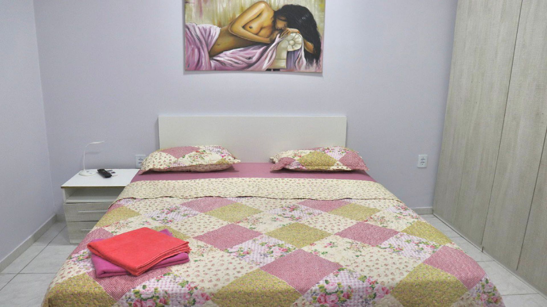 Un dormitorio con cama, almohadas, una mesita de noche y un cuadro en la pared.