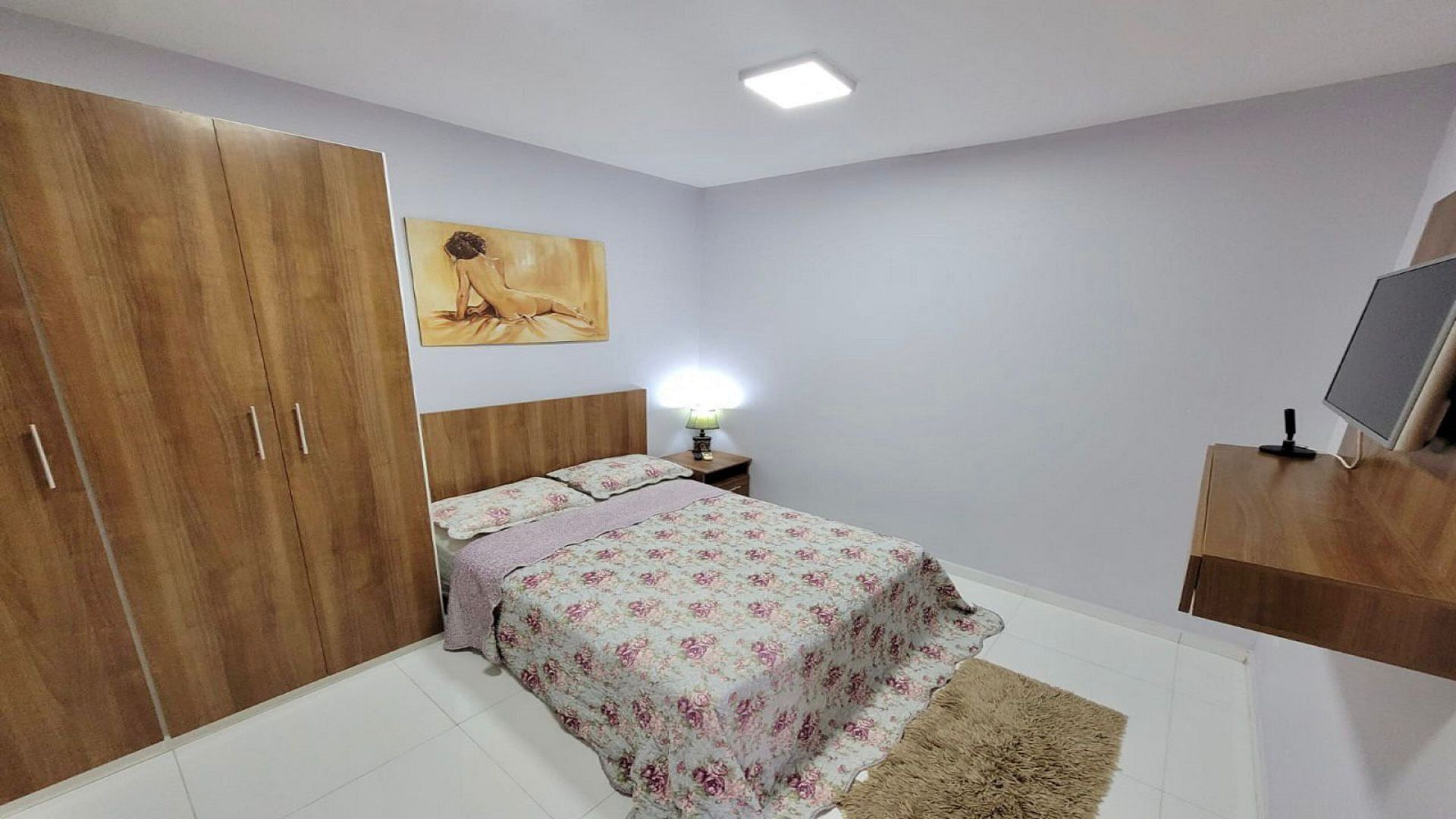 Una camera da letto con un letto, un armadio, un quadro, una lampada e un televisore.