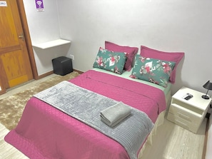 Une chambre à coucher avec un lit, des oreillers, une table de chevet, une lampe et un petit tabouret.
