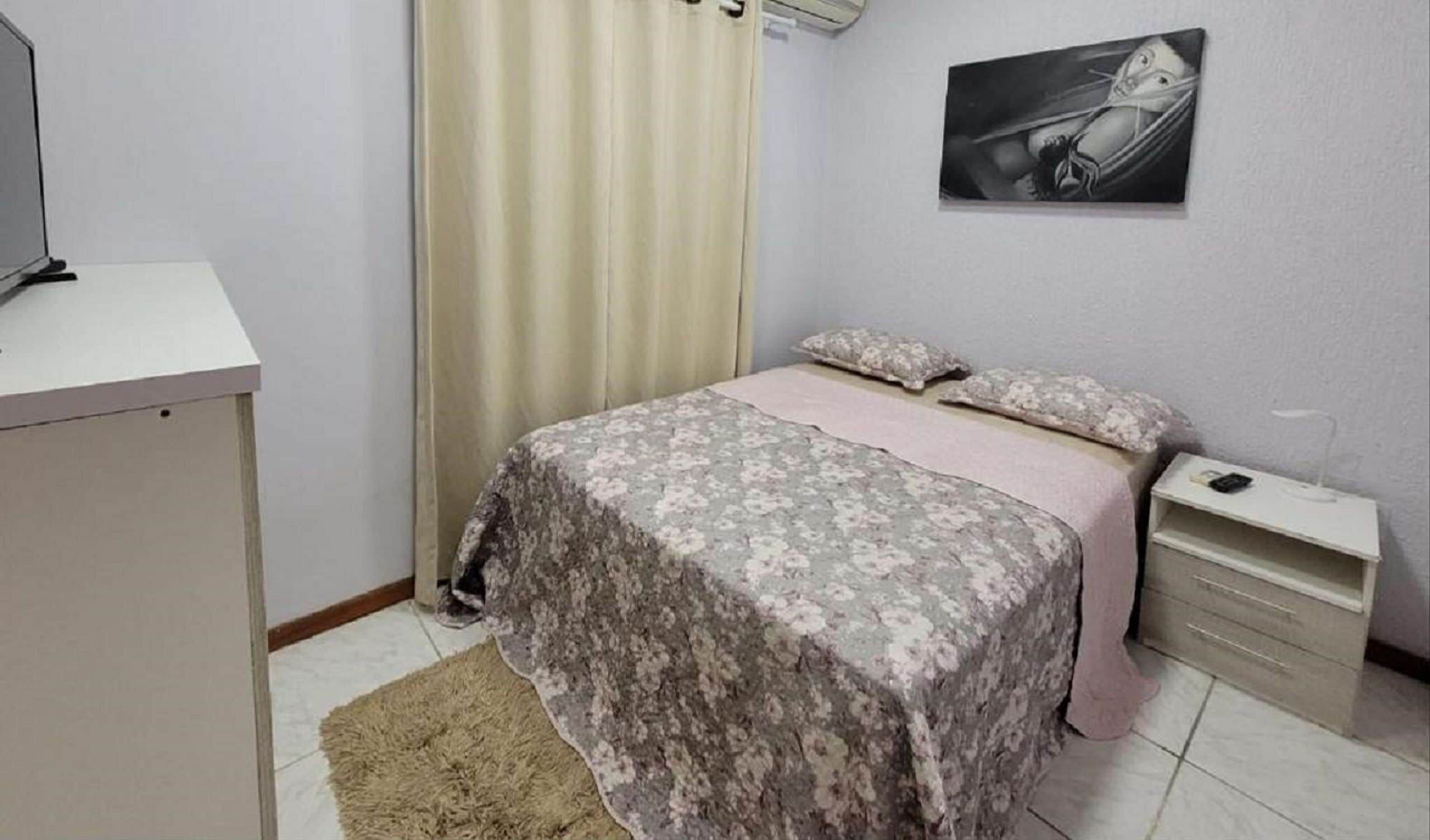 A bedroom with a bed, a desk, a nightstand, a lamp, and a painting on the wall.