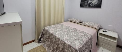 A bedroom with a bed, a desk, a nightstand, a lamp, and a painting on the wall.