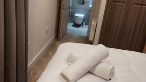 Una habitación de hotel con cama, baño visible a través de una puerta abierta y un armario de madera.