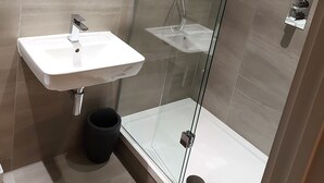 Un baño moderno con cabina de ducha de vidrio, un lavamanos blanco y un espejo sobre él.