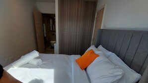 Habitación de hotel con cama, mesita de noche, armario y baño visible a través de una puerta abierta.