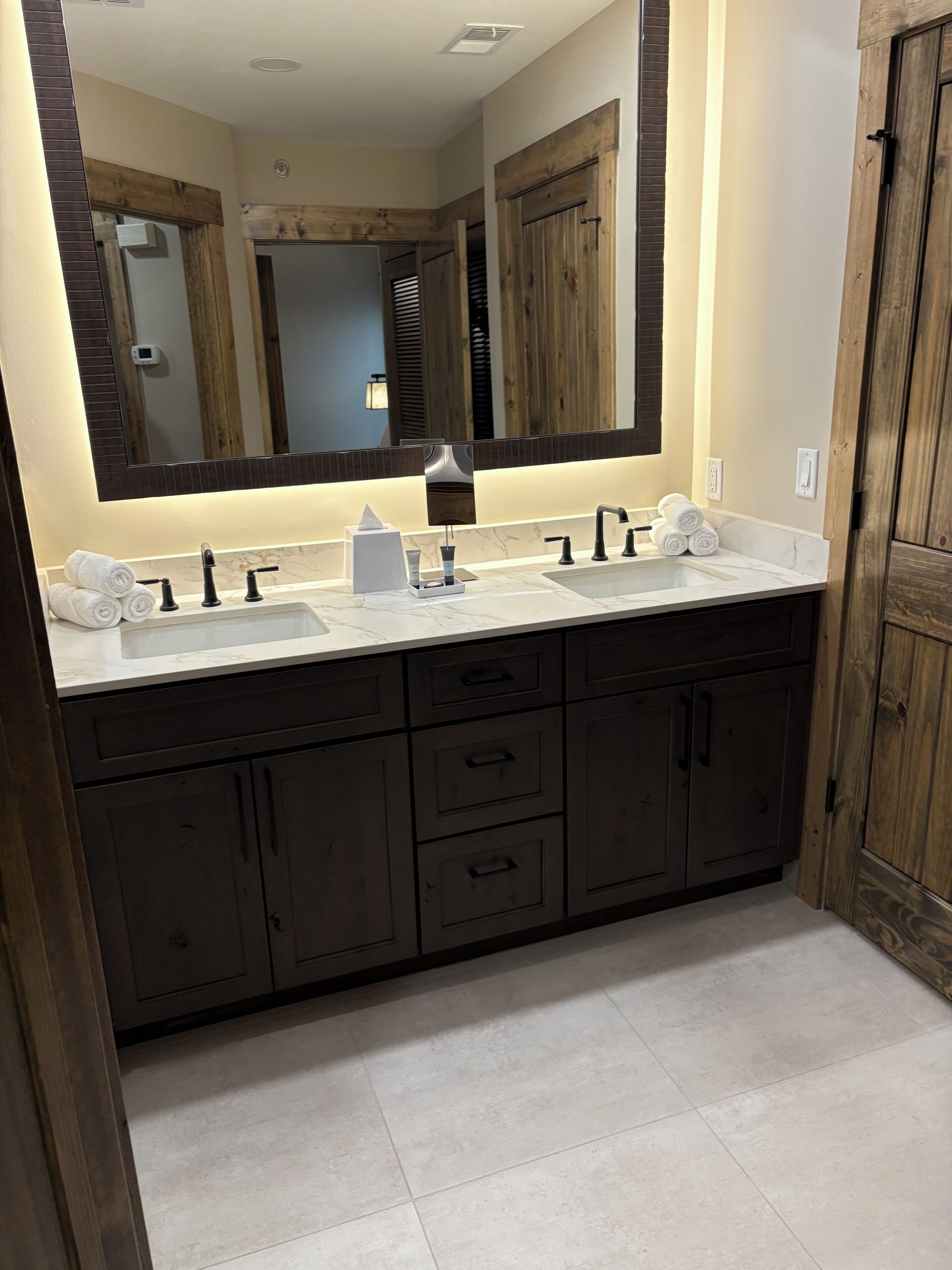 Un baño con lavamanos doble, muebles de madera oscura y un espejo grande.